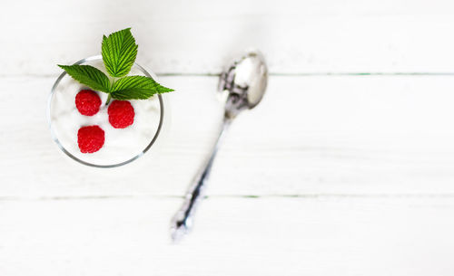 A glass with milk yogurt, ripe raspberries and a green leaf on a white wooden table 