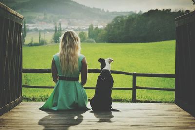 Rear view of woman with dog sitting on floorboard at farm