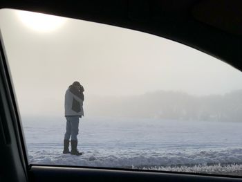 Man photographing on snowy field seen through car window