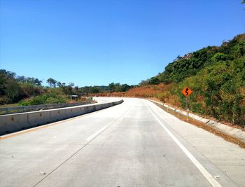 Road amidst trees against clear blue sky