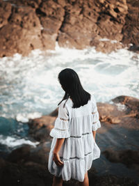 Rear view of woman standing on rock by sea