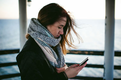 Side view of young woman using phone on pier over sea