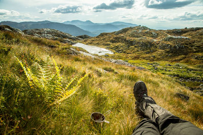 Low section of person relaxing on field against mountain