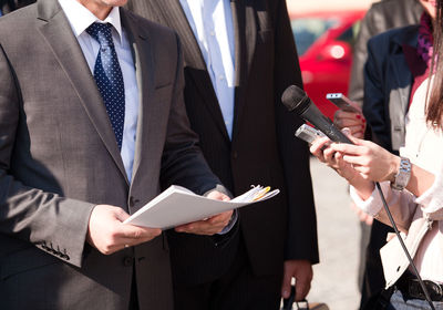 Midsection of journalist holding microphone in front of businessmen