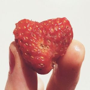 Close-up of strawberry holding ice cream over white background