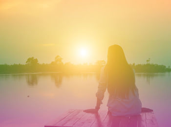 Rear view of woman looking at lake against sky during sunset