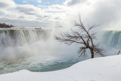 Scenic view of waterfall against cloudy sky during winter