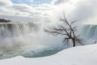 Scenic view of waterfall against cloudy sky during winter
