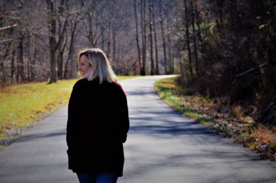 Rear view of happy woman walking on road in forest