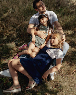 Portrait of father with two daughters sitting on field