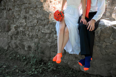 Low section of bride and groom sitting on stone wall