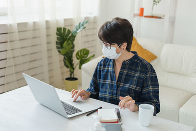 Senior woman wearing mask using laptop at office