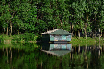 Wooden house on the river with reflection in it, surrounding by trees
