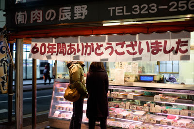 Midsection of friends standing near illuminated meat shop in city at night