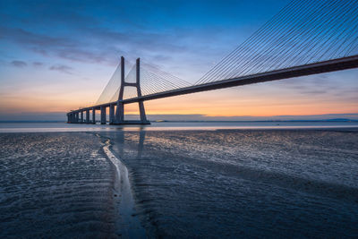 Suspension bridge over sea against sky during sunset