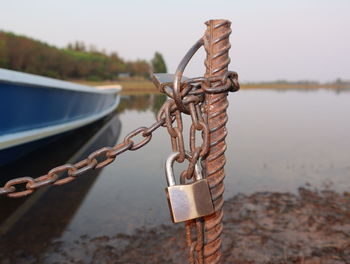 Close-up of chain tied up on metal by lake