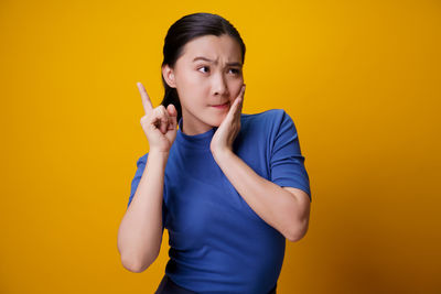 Portrait of young woman standing against yellow background