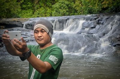 Portrait of man photographing while using mobile phone in water