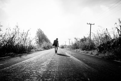 Rear view of man walking on road against sky
