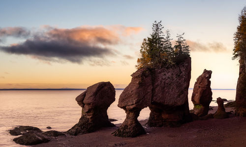 Rock formation on shore against sky during sunset