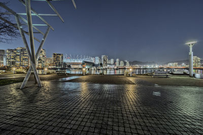 Illuminated city by river against sky at dusk