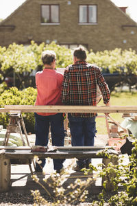 Rear view of senior couple standing by wooden plank at yard