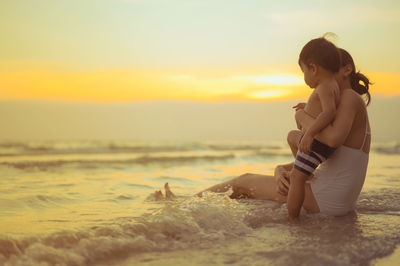 Woman sitting with son on beach during sunset