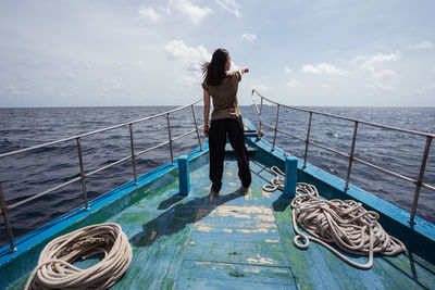 Full body back view of unrecognizable female traveler standing on ferry deck and pointing away while enjoying sea trip between islands in maldives