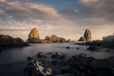 Rocks in sea against sky during sunset