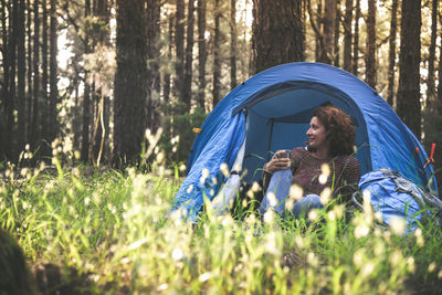 Mature woman looking away while sitting in tent at forest