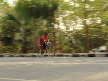 Blurred motion of man riding bicycle on road against trees