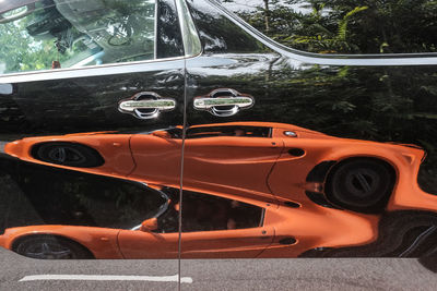 Reflection of an orange sports car against a black van doors