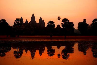 Reflection of silhouette trees on water against orange sky