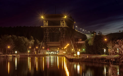 Illuminated bridge over river against sky at night