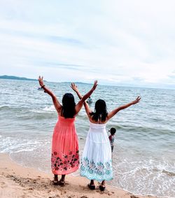 Rear view of women enjoying at beach against sky