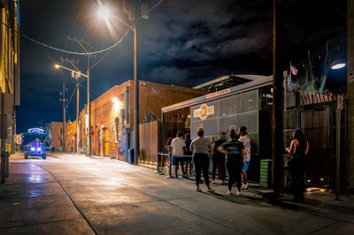 People on illuminated street amidst buildings in city at night