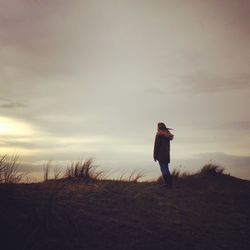 Woman standing on grassy field against cloudy sky during sunset
