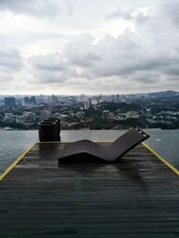 Deck chair on pier over river with cityscape in background