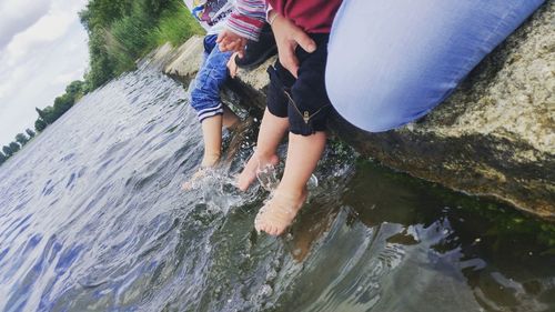 Low section of boy playing on rock by river