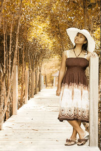 Thoughtful woman wearing straw hat looking up while standing on pier