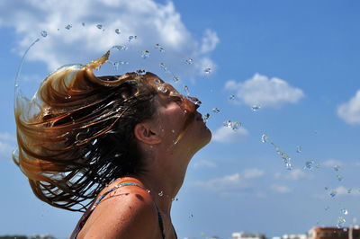Side view of woman tossing wet hair against sky