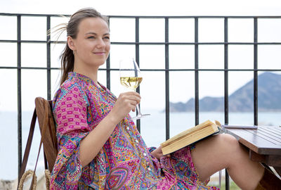 Young blonde sitting in a bar terrace reading a book with a glass of white wine