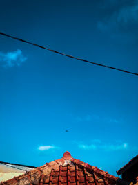 Low angle view of birds on roof against blue sky