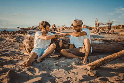 Young couple sitting on sand at beach against sky