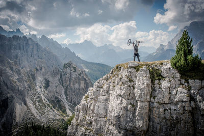 Man standing on cliff against cloudy sky