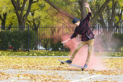 Teenage boy with powder paint skateboarding on footpath at park during autumn