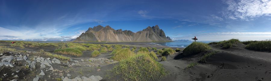 Panoramic view of man with surfboard standing on rock at beach against sky