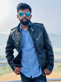 Portrait of young man wearing sunglasses while standing on mountain against sky