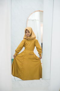 Portrait of young woman wearing hijab while standing against curtain