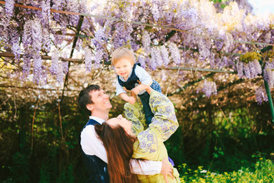 Playful parents holding child against tree